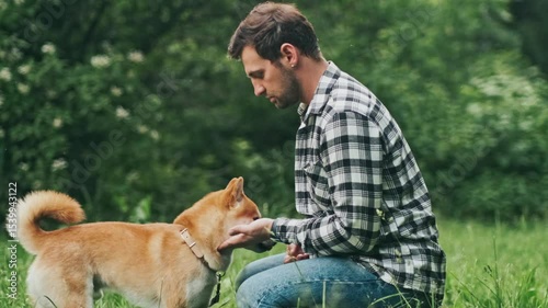 young man in plaid shirt playing training petting hugging and kissing his dog during summer park walk happy loving companionship concept lifestyle

