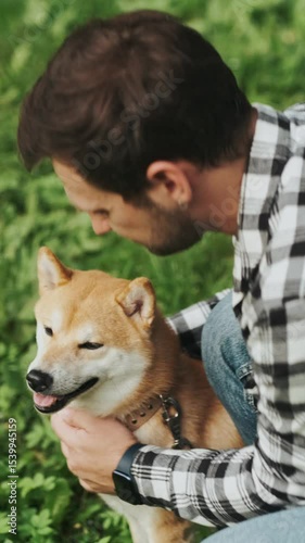 young man in plaid shirt playing training petting hugging and kissing his dog during summer park walk happy loving companionship concept lifestyle
