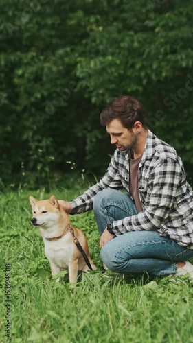 young man in plaid shirt playing training petting hugging and kissing his dog during summer park walk happy loving companionship concept lifestyle
