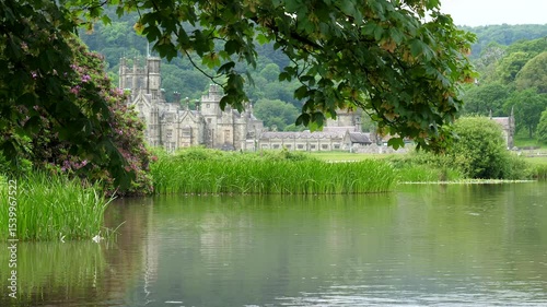 Part of Margam mansion view through tree branches in the park in South Wales, summer greenery and blossom around pond or lake. Local council property.