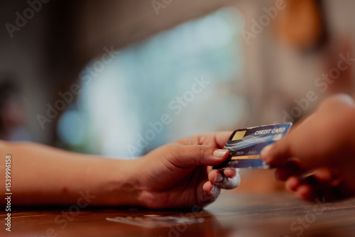 Close-up of hands using a credit card with payment terminal on wooden counter. Contactless transaction in small business setting.