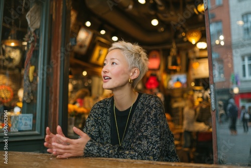 a Asian young woman with short blond hair talking passionately during an interview or conversation. A woman is sitting at a table in a cafe. 