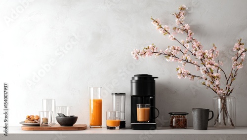 Minimalist kitchen counter scene with coffee maker, juice, glasses, and cherry blossoms