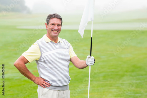 Senior African American man holding flagstick and smiling on putting green in vest and golf glove