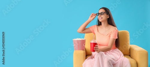 Young woman in armchair, with 3D glasses, popcorn and soda watching movie on ...