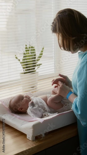 Vertical shot of young woman having fun playing with her newborn baby after changing diapers
