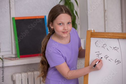 Young girl joyfully solving math problems on a chalkboard in a bright classroom setting