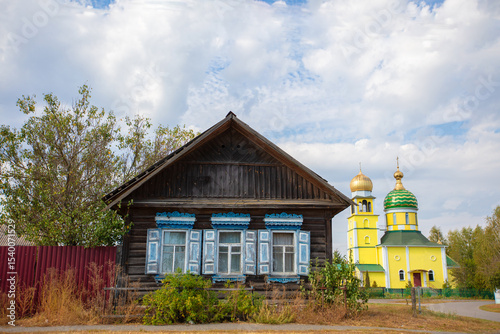 Traditional wooden house beside a colorful church in a rural setting during daytime
