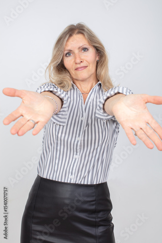 Woman in striped shirt extends arms in an inviting gesture against a plain background