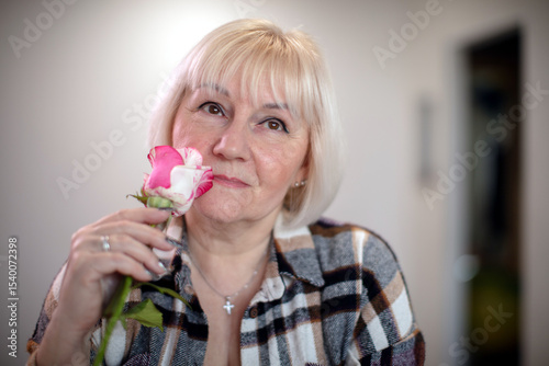 Woman holding a pink and white rose while looking thoughtfully in a cozy indoor setting