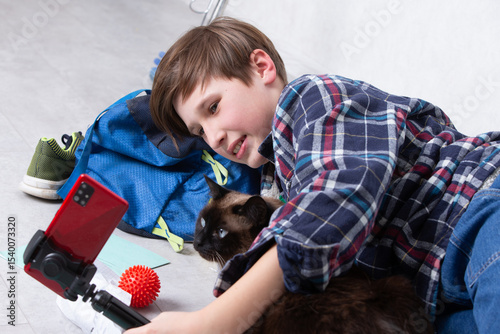 Young boy enjoys playful moment with cat while recording on smartphone in cozy indoor setting