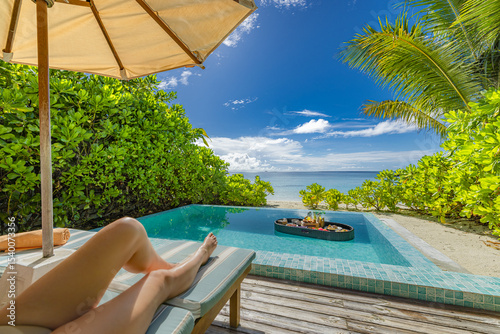 Relaxing sexy woman legs relaxing with floating breakfast in private pool at luxury beach resort. Tranquil sun chairs beds umbrella under sunny sky sea sand. Tropical vacation paradise calming travel