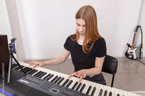 Young woman playing keyboard in a bright music studio while focusing on her performance