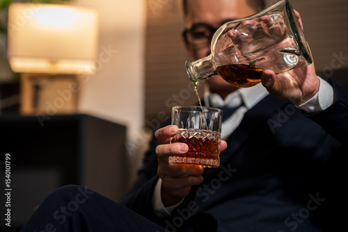 Businessman holding a glass of whiskey, sitting and drinking in a room