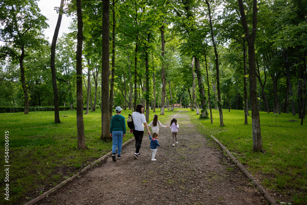 Fototapeta premium Family enjoying a walk in a serene green park surrounded by tall trees