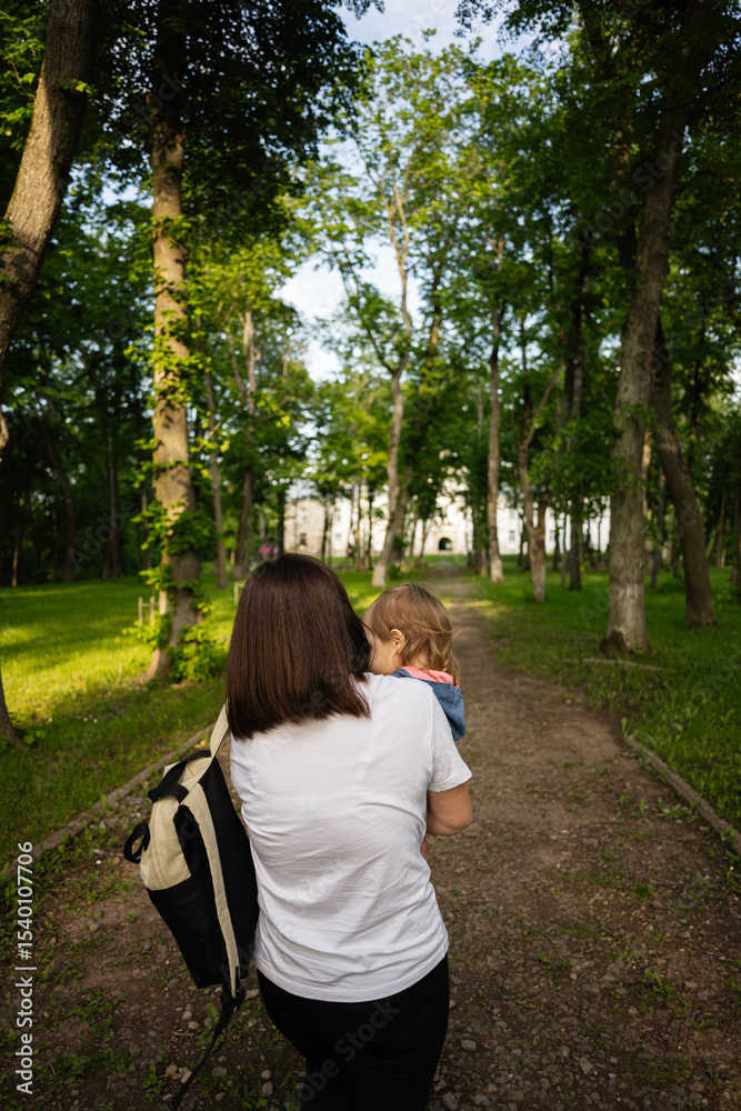 Naklejka premium Mother and child walking through lush green park towards historic building