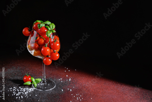 Cherry tomatoes on vine with basil in glass, surrounded by sea salt on dark textured surface, modern conceptual food art representing plant-based nutrition