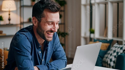 Man smiling on his laptop. Man working on a laptop in an office. A male focused on a remote. A man grinning at his laptop lifestyle.