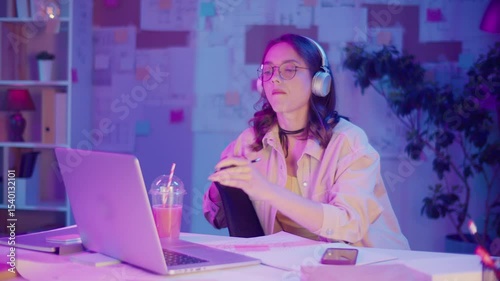 Gen Z Lifestyle, Digital Multitasking, Neon Mood. Teen Girl Draws While Listening Music and Watching Laptop Screen. Personal Expression in Creative Chaos of Modern Youth in Neon Light