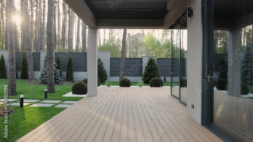 Terrace near modern house. Terrace with wooden floor, slatted roof, large window, near garden and greenery in the yard. Luxury house. Sunset.