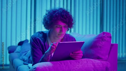 Digital Detox, Mental Health, Focus Mode. Man Relaxes on Sofa Using Tablet, Possibly Watching Streaming Content or Reading. Everyday Self-Care and Slow Living in the Digital Age