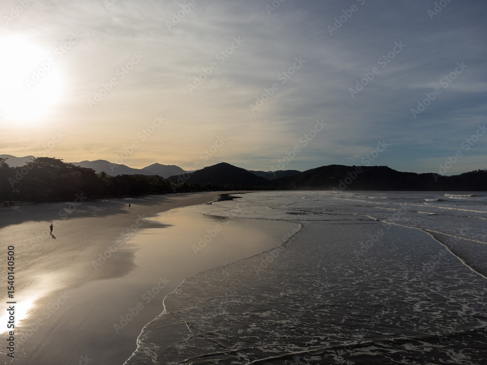 Fototapeta premium beautiful reddish sunrise on the beach with small waves and mountain horizon