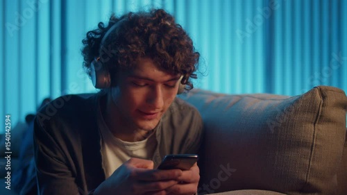 Digital Detox, Mental Health, Focus Mode. Man Relaxes on Sofa Scrolling Phone, Possibly Listening a Podcast or Browsing. Everyday Self-Care and Slow Living in the Digital Age