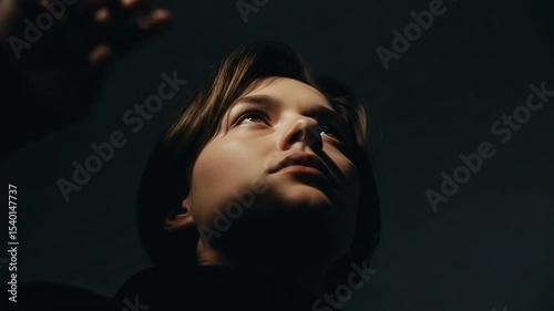 Young Woman Portrait in Dark Light Looking Up with Hand Close Up on Black Background