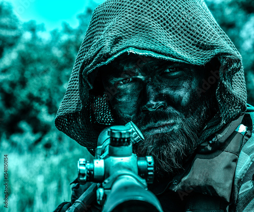 Intense sniper with a hood and camouflage face paint aiming a rifle, set against a blurred natural background with a blue color tone.