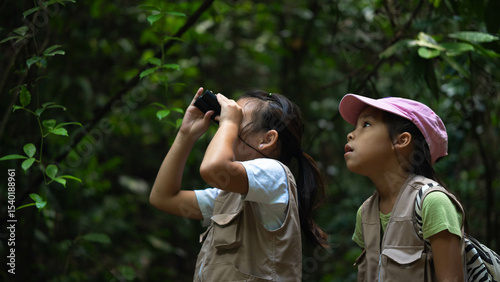 Smiling kids exploring nature. Cute little girl learning about nature with binoculars in the forest during a summer day together.