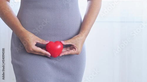 Close-up of a woman holding a red heart-shaped object, representing vaginal discharge, menopause, reproductive system care, and gynecological health awareness