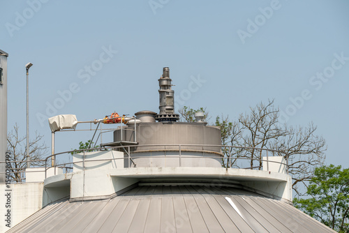 Closeup of the top of a unit of a biogas enterprise. Trees in the background. Blue sky.