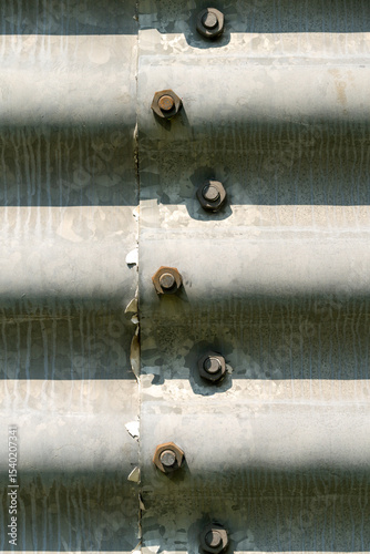 Corrugated metal sheets at a factory building fixed with heavy nuts and bolds. Signs of weathering. Sunshine casting shadows.