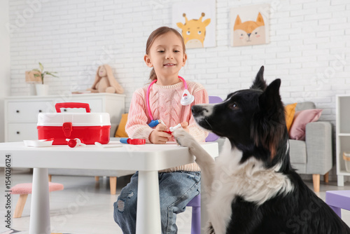 Cute little girl with toys and dog playing doctor at home photo