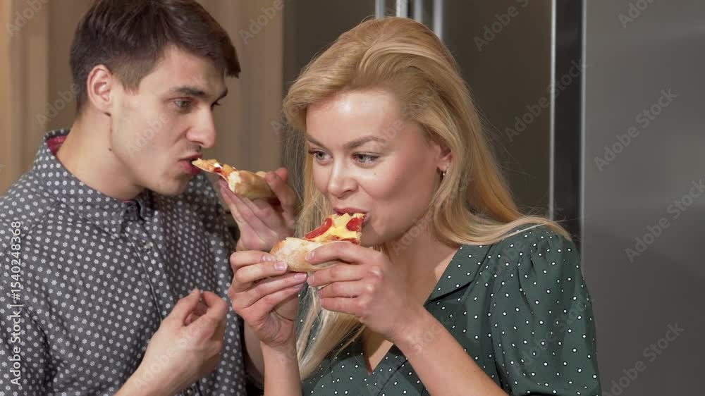 Joyful couple savoring delicious pizza in their cozy new kitchen Joyful couple savoring delicious pizza in their cozy new kitchen