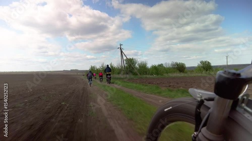Active tourists cycling down the country road on sunny day. Bike, group and riders cycling on dirt road with scenic view. Travel, teamwork and adventure.
