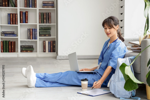 Female medical intern studying with laptop on floor in library