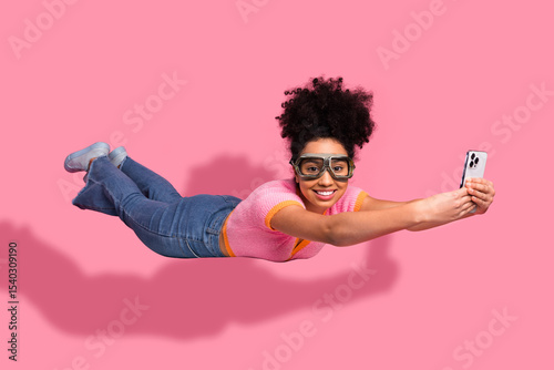 Принти на полотні Charming young woman posing in a flying superhero gesture holding a smartphone,