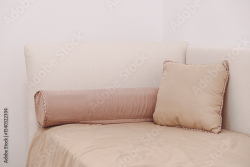 Beige sofa corner with plush and bolster pillows creates a cozy and inviting seating area. The soft texture of the pillows enhances comfort, adding warmth to the minimalist design