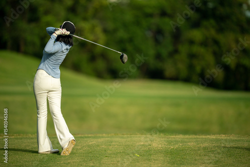 A woman is swinging a golf club on a grassy field