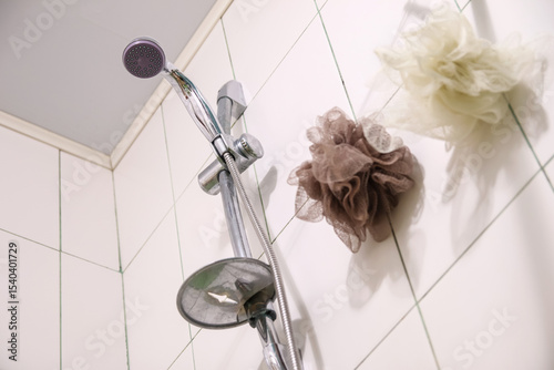 A silver shower head and a white washcloth on clean tiles in a modern bathroom, ready for a refreshing shower. Spotless white tiles frame a silver shower head and a fresh washcloth