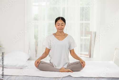 Asian calm woman practicing yoga meditation peacefully indoors, sitting cross legged on bed, relaxing mind and body in bright, serene bedroom environment Free Download Asian calm woman practicing yoga meditation peacefully indoors, sitting cross legged on bed, relaxing mind and body in bright, serene bedroom environment - GFXLoad