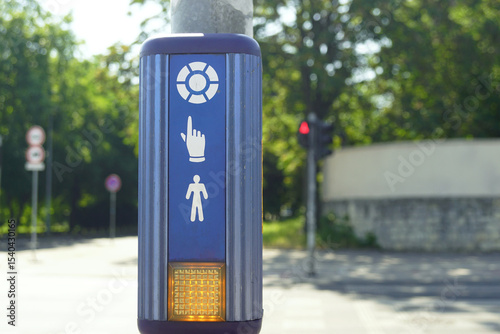 A close-up photo of a device for people who want to cross the road to the other side of the street. A pedestrian device with a button against the background of a road and a red traffic light