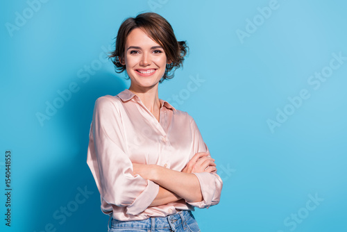 Charming young businesswoman with a confident smile in a satin blouse against a vibrant blue background