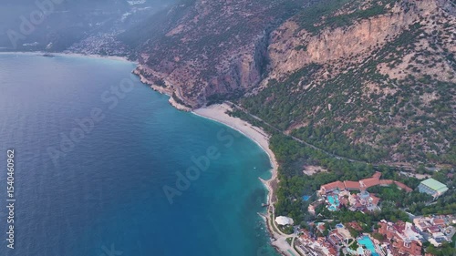 Aerial drone view revealing turquoise waters meeting lush green mountains along dramatic coastline of cirali, turkey, highlighting scenic beach and resort nestled in pristine natural landscape