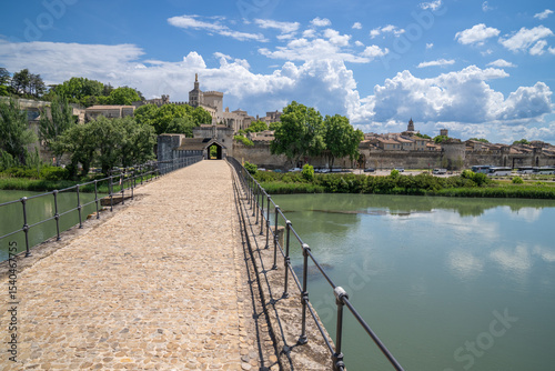 A view of the city of Avignon from the bridge over the river Rhone. Ble sky with white fluffy clouds and a calm river invokes a tranquil peaceful environment