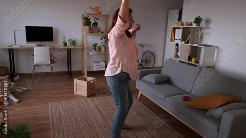Joyful elderly woman wearing headphones dances and enjoys music in her modern, cozy living room, expressing freedom and happiness in retirement