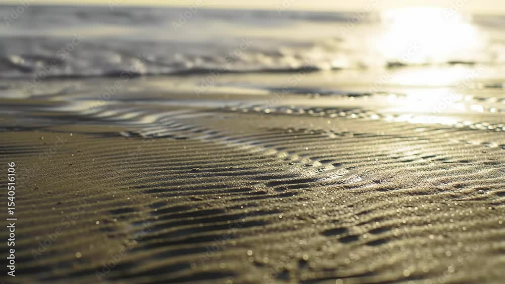 Close-up of wet sand at the beach, patterns from receding water. Sunlight reflects on the tiny grains
