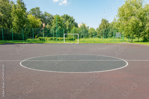 Soccer field with a white line in the middle. The field is empty. The sky is blue and the trees are green