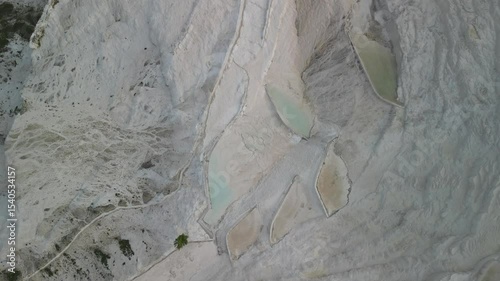 A drone spirals downward over white travertine in Pamukkale. Thermal pools of Turkiye seen from above in a spinning descent. Turkiye's natural wonder beautifully framed. photo